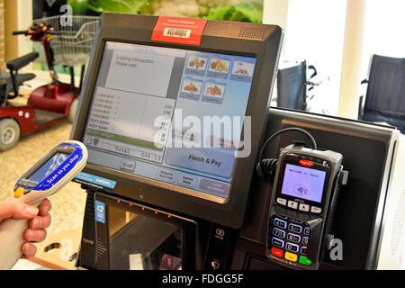 L'acquirente Tesco mira alla sua scansione come dispositivo di acquisto per caricare gli articoli di acquisto sullo schermo per il pagamento al check-out self-service fino a Londra Inghilterra Regno Unito Foto Stock