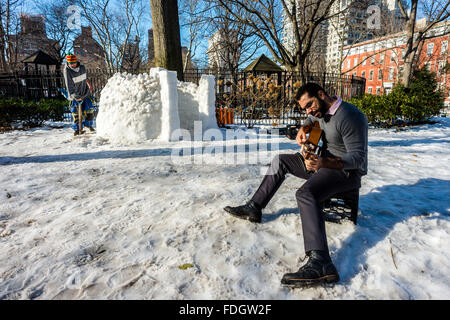 New York, NY, Stati Uniti d'America - 31 Gennaio 2016 - un uomo costruisce un igloo mentre un altro suona la chitarra su un pomeriggio invernale in Washington Square Park ©Stacy Rosenstock Walsh/Alamy Foto Stock