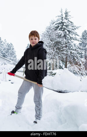 Ragazzo giovane spalare la neve fuori dell'entrata anteriore a casa sua Foto Stock