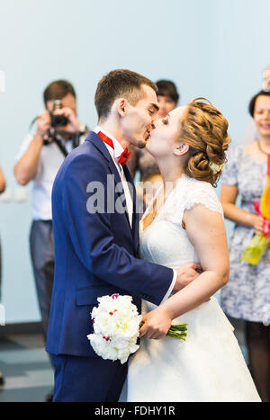 I giovani sposi novelli baciare e godendo di momento romantico insieme al ricevimento di nozze al di fuori, ospiti di nozze in background Foto Stock
