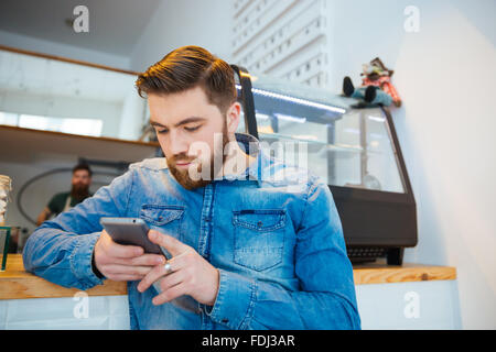 Bel giovane utilizza lo smartphone in cafe Foto Stock