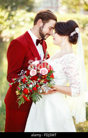 Marsala wedding couple, bride and groom embracing, dark red color style design. Suit with maroon bow tie, white dress, bridal bo Foto Stock