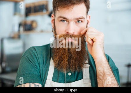Closeup ritratto del bel giovane con la barba in grembiule bianco toccando i suoi baffi Foto Stock