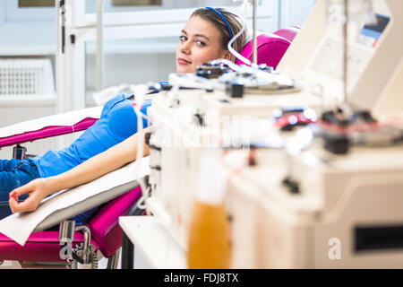 Piuttosto, giovane donna donazione del sangue/plasma. Che stabilisce mentre la procedura avviene (toni di colore immagine; shallow DOF) Foto Stock
