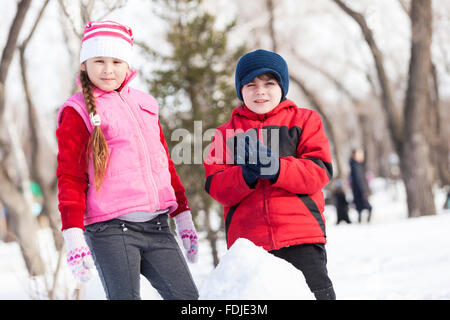 Carino un ragazzo e una ragazza la costruzione di pupazzo di neve in inverno park Foto Stock