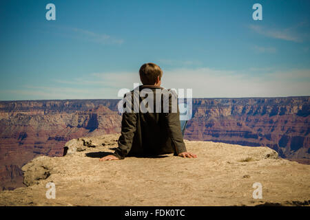 Vista posteriore di un giovane uomo seduto sulla mensola e Grand Canyon, Arizona, america, STATI UNITI D'AMERICA Foto Stock