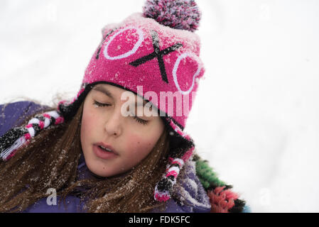 Ragazza distesa nella neve con gli occhi chiusi Foto Stock