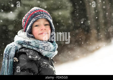 Ragazzo sorridente in piedi nella foresta nella neve Foto Stock