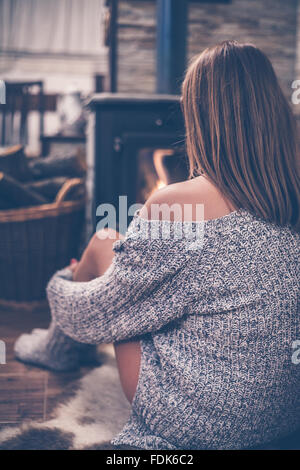 Vista posteriore di una donna seduta davanti a una stufa a legna Foto Stock