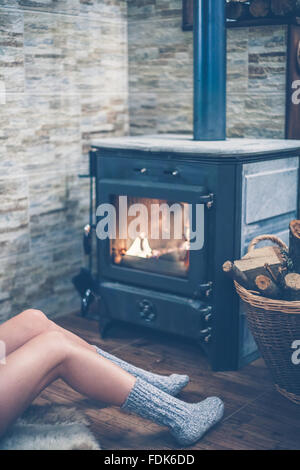 Donna seduta davanti a una stufa a legna Foto Stock