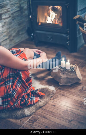 Donna seduta davanti a una stufa a legna e candele Foto Stock