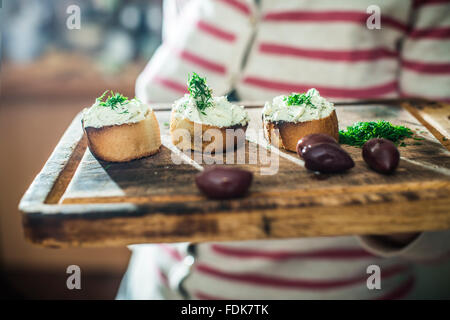 Donna che mantiene tagliere con bruschetta con morbida crema di formaggio e olive Foto Stock