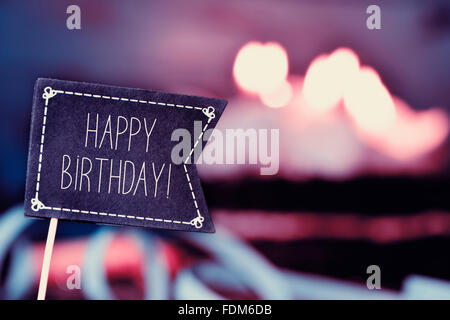 Primo piano di una bandiera nera a forma di cartello con il testo buon compleanno e una torta di compleanno con candele accese in background Foto Stock