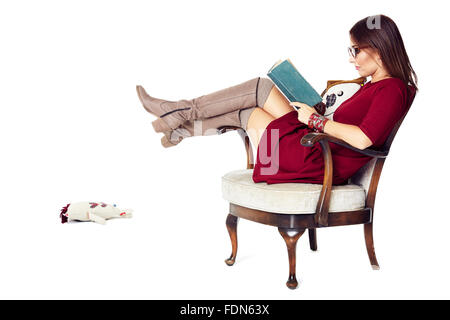 Donna attraente la lettura di un libro comodamente seduti in una vecchia sedia. Foto Stock