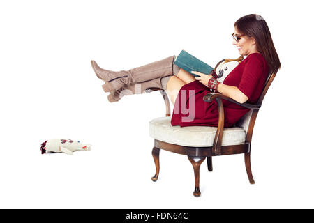 Donna attraente la lettura di un libro comodamente seduti in una vecchia sedia. Foto Stock