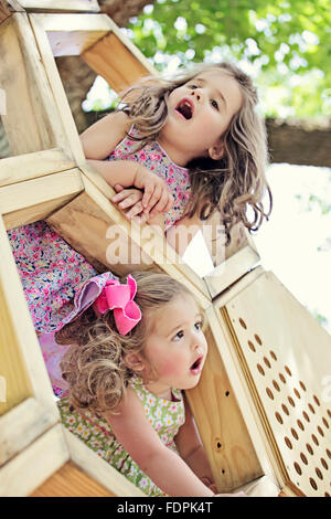 Due giovani ragazze popping le loro teste fuori di una struttura in legno con sguardi di stupore sui loro volti. Foto Stock