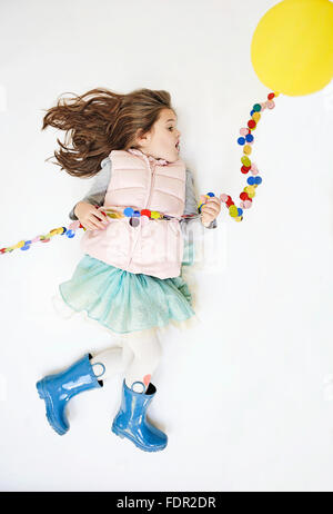 Bambina fingendo di prendere il volo per mezzo di un palloncino giallo. Foto Stock