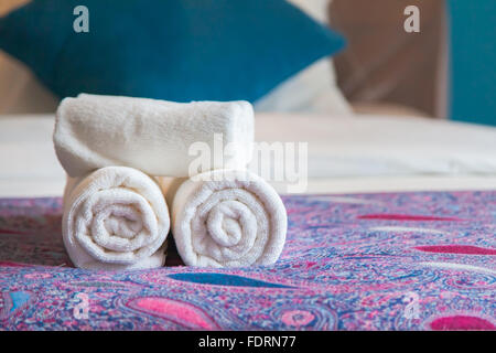 White asciugamano da bagno arrotolata su un letto in camera d'albergo. Il benvenuto agli ospiti. Foto Stock