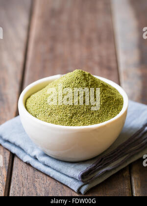 Moringa polvere (super) in una ciotola bianco su un rustico in legno sfondo. Orientamento verticale. Foto Stock