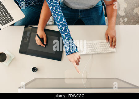 Vista dall'alto ritagliata colpo di un uomo con tavoletta grafica digitale con lo stilo e la tastiera del computer, con la donna puntando al computer mo Foto Stock
