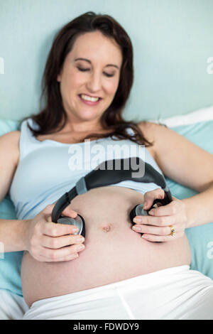 Donna incinta mettendo le cuffie sul suo ventre Foto Stock