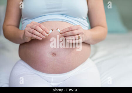 Donna incinta il taglio di una sigaretta in due Foto Stock