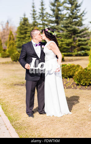 Sposa e lo sposo holding bouquet e parola in legno amore Foto Stock