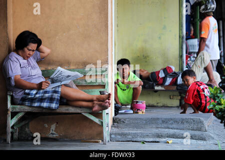 Un senior lady leggendo un giornale e, dietro, bambini che giocano. Una normale scena di vita nel centro di Yogyakarta, Indonesia Foto Stock