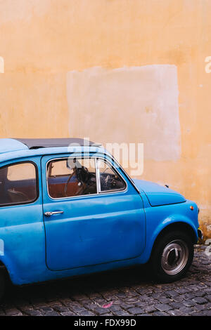 Un luminoso blu vintage Fiat 500 parcheggiato contro una parete gialla in Roma, Italia Foto Stock