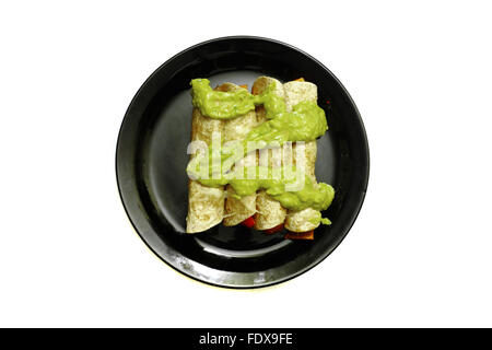 Burrito cotto ricoperto in salsa guacamole su una piastra nera fotografati contro uno sfondo bianco Foto Stock