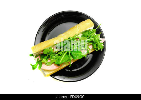 Una baguette piena di prosciutto e lattuga su una piastra nera fotografati contro uno sfondo bianco Foto Stock