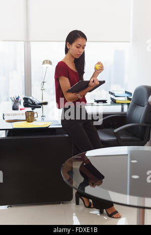 Lavoratore di ufficio appoggiato sulla scrivania. La donna si legge un messaggio di posta elettronica sul computer tablet e detiene un anti-stress sfera gialla. Ella si sente stres Foto Stock