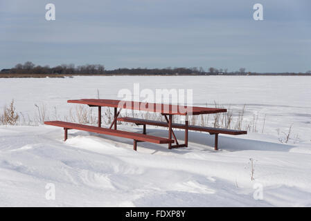 Un tavolo da picnic sulle sponde del lago grande sta diventando sepolto in un cumulo di neve in una fredda giornata invernale. Foto Stock