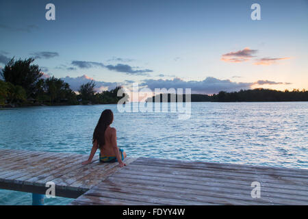 Donna seduta sul molo al tramonto, Hauru Point, Mo'Orea, Isole della Società, Polinesia Francese Foto Stock