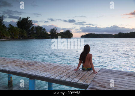 Donna seduta sul molo al tramonto, Hauru Point, Mo'Orea, Isole della Società, Polinesia Francese Foto Stock
