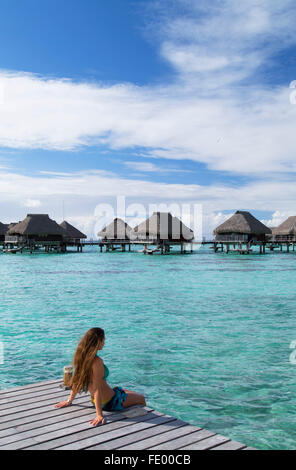 Donna seduta sul molo al Hilton Mo'orea Lagoon Resort Hotel, Moorea, Isole della Società, Polinesia Francese Foto Stock