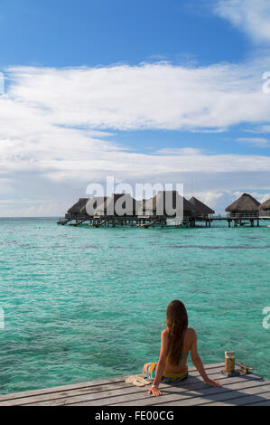 Donna seduta sul molo al Hilton Mo'orea Lagoon Resort Hotel, Moorea, Isole della Società, Polinesia Francese Foto Stock