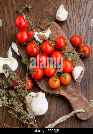 Organici di pomodorini con aglio e timo erba su una tavola di legno Foto Stock