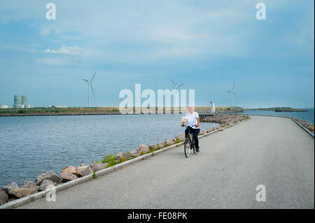 Uomo in bicicletta lungo l'isola di Helgoland Badeanstalt spiaggia e piscina a Copenaghen in Danimarca con turbine eoliche in background Foto Stock