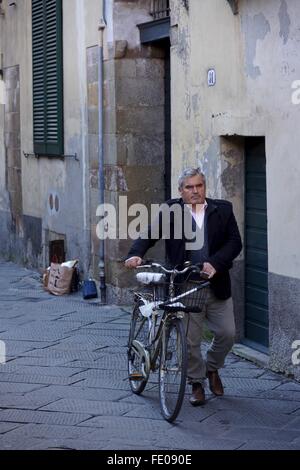 Un uomo cammina la sua moto attraverso le strade Foto Stock