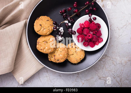 Stile Americano White Chocolate Chip Cookie ob la piastra nera servito con lamponi sulla superficie di marmo, i cookie con mirtilli rossi Foto Stock