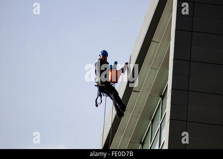 Detergenti per finestre sospesa in alto in sede i cavi elettrici sulle corde di cordata lavaggio appartamento di lusso windows a Dundee, Regno Unito Foto Stock