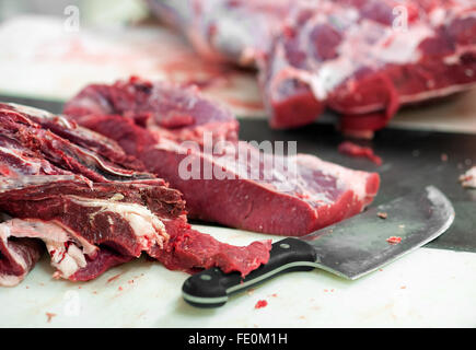 Close up dei tagli di carne cruda sul tavolo affollato con grande coltello in food processing facility Foto Stock