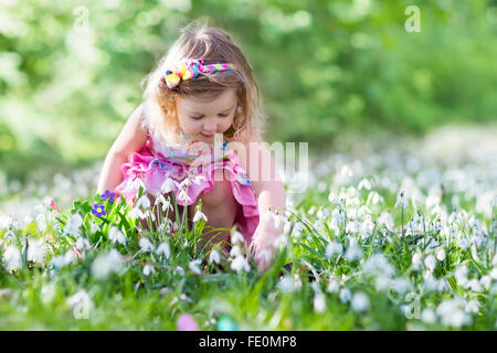 Bambina che si divertono sull'uovo di Pasqua Caccia. I bambini in primavera in fiore giardino con crocus e snowdrop fiori Foto Stock