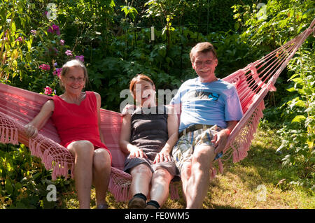 Tre molto felice cercando persone di mezza età, giovane e amico, seduto su un amaca nel pomeriggio di sole Foto Stock