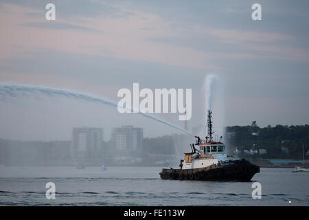 Il Atlantic Oak rimorchiatore flessibili spara in aria come la Queen Mary 2 vele fuori Halifax, Canada. Foto Stock