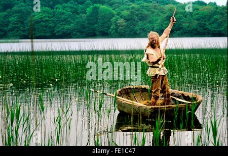 Il neolitico rievocazione. Età della pietra uomo con corna corno di pesce a punta di lancia in pelle d'animale coracle sul lago. Kilmartin, Scozia Foto Stock