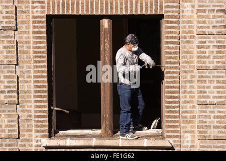 Operaio edile w/ un grande uno scalpello e un martello la rimozione e la sostituzione di una finestra in legno frame da un edificio in mattoni Foto Stock