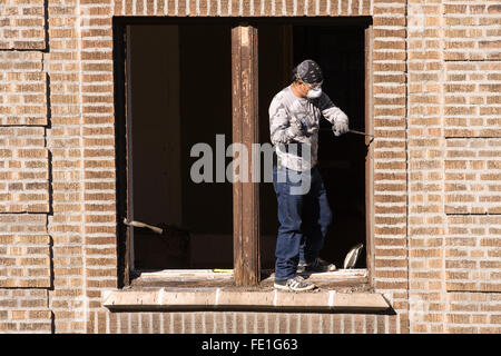 Operaio edile w/ un grande uno scalpello e un martello la rimozione e la sostituzione di una finestra in legno frame da un edificio in mattoni Foto Stock