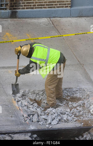 Operaio edile rimuovere manualmente il calcestruzzo rotto i detriti da un foro del marciapiede con una pala (FE1G87, Fe1G8A, FE1G8C) Foto Stock